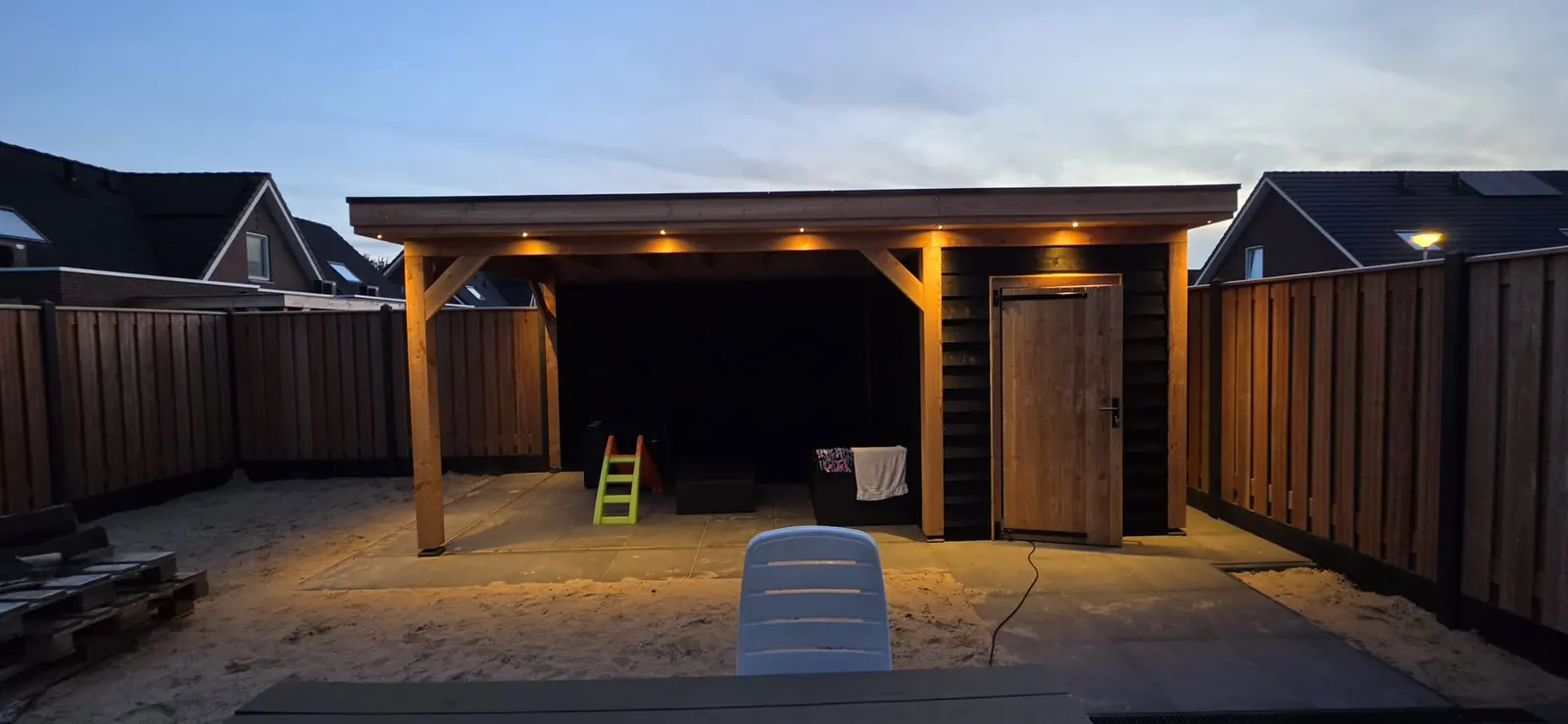 Brede houten overkapping in de schemer met verlichting